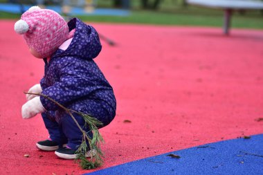 Yavru kız soğuk sonbahar kışında elinde ağaç dallarıyla çömeliyor.
