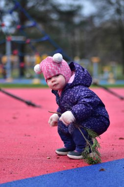 Yavru kız soğuk sonbahar kışında elinde ağaç dallarıyla çömeliyor.