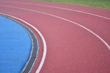 Beyaz çizgileri olan kırmızı koşu yolu eğrisi, sol tarafta mavi spor sahası ve sağ tarafta yeşil çimen
