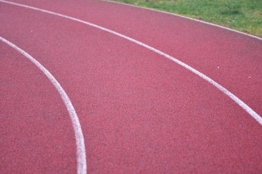Beyaz çizgiler ve sağ tarafta yeşil çimenler olan kırmızı koşu yolu eğrisi