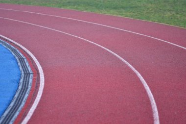 Beyaz çizgileri olan kırmızı koşu yolu eğrisi, sol tarafta mavi spor sahası ve sağ tarafta yeşil çimen