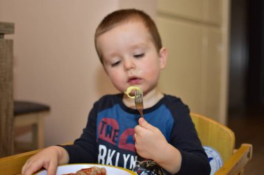 Küçük çocuk öğle yemeğini çatalla yiyor.