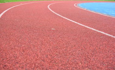 Sol tarafta çimen ve sağ tarafta mavi spor sahası olan kırmızı koşu pisti.