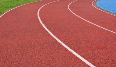 Beyaz çizgiler ve sağ tarafta yeşil çimenler olan kırmızı koşu yolu eğrisi