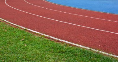 Sol tarafta çimen ve sağ tarafta mavi spor sahası olan kırmızı koşu pisti.