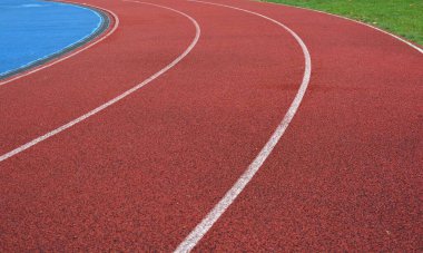 Beyaz çizgileri olan kırmızı koşu yolu eğrisi, sol tarafta mavi spor sahası ve sağ tarafta yeşil çimen