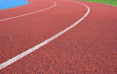 Beyaz çizgileri olan kırmızı koşu yolu eğrisi, sol tarafta mavi spor sahası ve sağ tarafta yeşil çimen