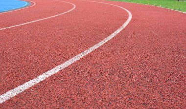 Beyaz çizgiler ve sağ tarafta yeşil çimenler olan kırmızı koşu yolu eğrisi