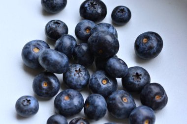 Taze yaban mersinleri beyaz masaya yayılmış. Üst manzara makrosu yakın. Beyaz yüzeyde bir sürü böğürtlen.