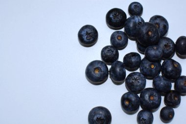 Taze yaban mersinleri beyaz masaya yayılmış. Üst manzara makrosu yakın. Beyaz yüzeyde bir sürü böğürtlen.