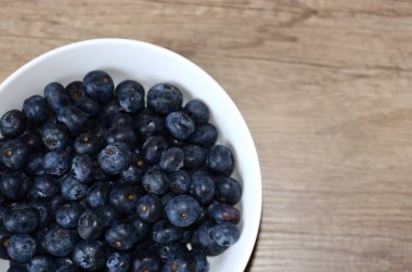Ahşap masa manzaralı bir kase taze yaban mersini. Ahşap yüzeyde mavi böğürtlen kasesi.