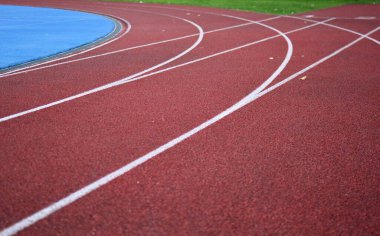 Beyaz çizgileri olan kırmızı koşu yolu eğrisi, sol tarafta mavi spor sahası ve sağ tarafta yeşil çimen