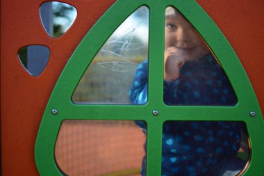 Küçük çocuk oyuncak evin penceresinden izliyor ve güneşli bir günde elinde neşeyle kapıyı çalıyor. Çocuk halk parkında oynuyor..