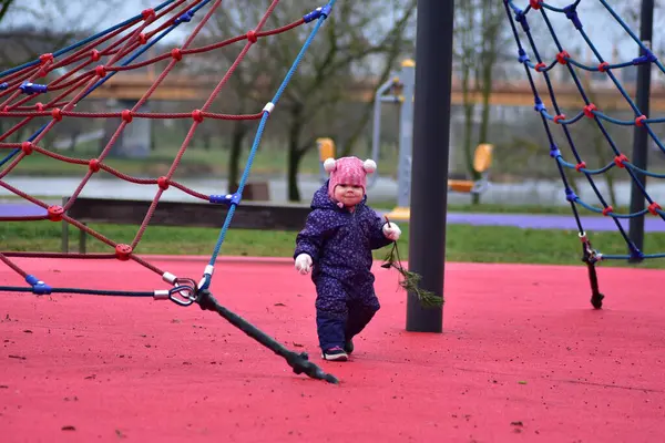 Yavru kız, soğuk sonbahar kışında, çocuk parkında iplere tırmanıyor ve ağaç dallarını tutuyor.