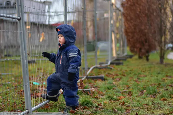 Sonbaharda şantiyeyi gözetleyen kapüşonlu meraklı bir çocuk. Yeni yürümeye başlayan çocuk çitin yanında duruyor. Çocuk inşaatın nasıl işlediğini izliyor.