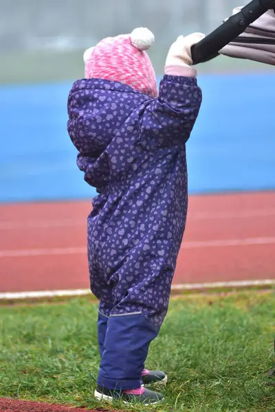 Küçük kız kışın spor sahasında yürüyor. Dışarıda eğlenceli aktiviteler yapıyor. Kışlık giysili çocuk bebek arabası itiyor.