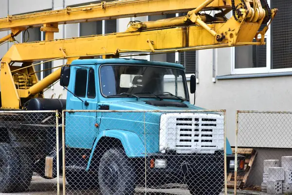 Eski usul Rus vinç kaldırıcı vinç servisi okul binasının yanında duruyor. Sovyet mirası paslı vinç kamyonu.