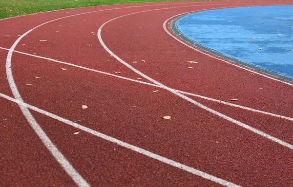 Sol tarafta çimen ve sağ tarafta mavi spor sahası olan kırmızı koşu pisti.