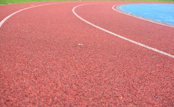 Sol tarafta çimen ve sağ tarafta mavi spor sahası olan kırmızı koşu pisti.