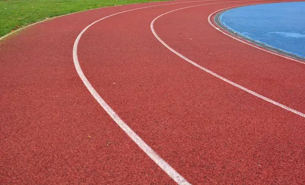 Sol tarafta çimen ve sağ tarafta mavi spor sahası olan kırmızı koşu pisti.