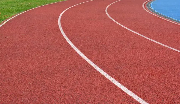 Beyaz çizgiler ve sağ tarafta yeşil çimenler olan kırmızı koşu yolu eğrisi