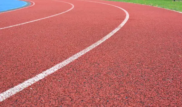 Beyaz çizgiler ve sağ tarafta yeşil çimenler olan kırmızı koşu yolu eğrisi