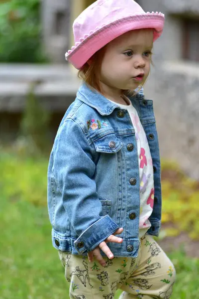 Pembe şapkalı ve kot ceketli küçük kız baharda dışarıda yürüyor. Küçük kız, açık havada yakın portre..