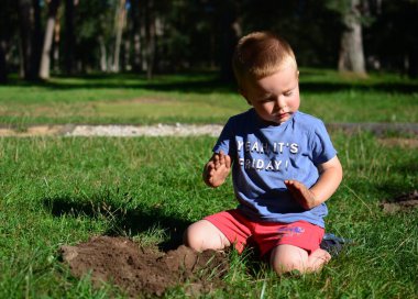 Küçük çocuk güneşli bir yaz gününde parkta toprak kazıp oynuyor. Çocuk dışarıda eğleniyor..