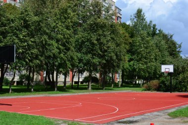 Güneşli yaz günlerinde eski apartman bloklarının yakınında lastik kaplamalı yeni açık hava basketbol sahası.