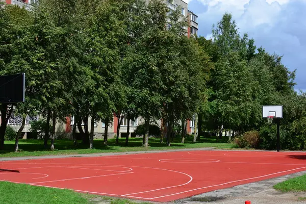 Güneşli yaz günlerinde eski apartman bloklarının yakınında lastik kaplamalı yeni açık hava basketbol sahası.
