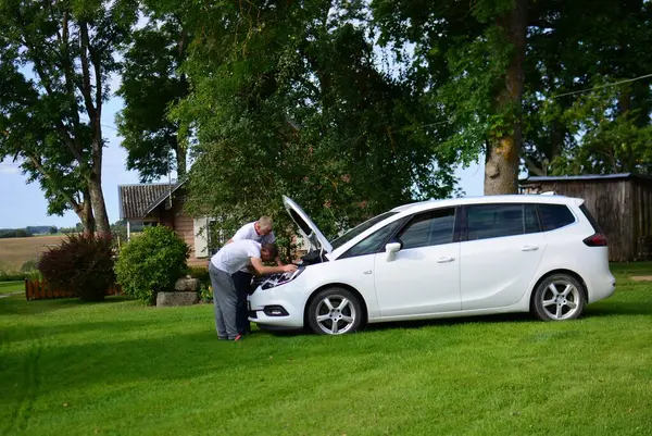 Orta yaşlı ve yaşlı adamlar yaz günü beyaz minivanları teftiş ediyor. Kırsalda motor kaputunun altına bakan iki adam var. Erkekler arabalarını kendileri tamir ediyorlar..