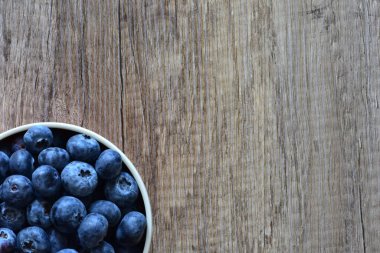 Tahta bir masada taze yaban mersinleriyle dolu bir kase, doğal ve sağlıklı bir yaşam tarzını yakalıyor. Yemek, organik ve mevsimlik temalar için ideal. Üst görünüm, yüksek çözünürlüklü resim.