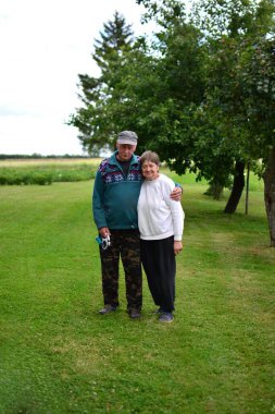 Kıdemli çift yaz günü kırsal alanda mutlu bir şekilde yan yana sırıtıyor. Yaşlı adam kırsalda yaşlı karısına sarılıyor. 65 yaşından büyük çiftçilerin sıradan köy manzaralı portresi.