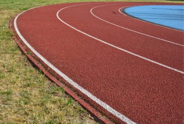 Sol tarafta çimen ve sağ tarafta mavi spor sahası olan kırmızı koşu pisti.