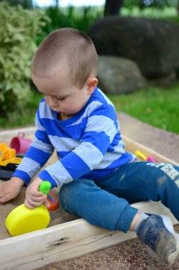 Küçük çocuk arka bahçedeki kum havuzunda oynuyor. Çocuk yazın dışarıda oyuncak tavayla kum yemeği yapıyor..