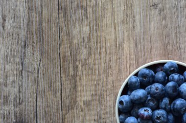 Tahta bir masada taze yaban mersinleriyle dolu bir kase, doğal ve sağlıklı bir yaşam tarzını yakalıyor. Yemek, organik ve mevsimlik temalar için ideal. Üst görünüm, yüksek çözünürlüklü resim.