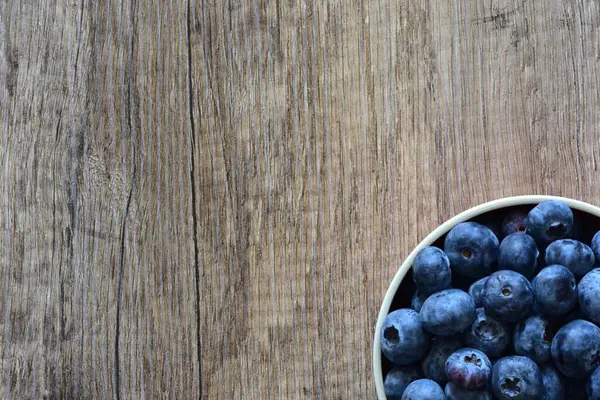 Tahta bir masada taze yaban mersinleriyle dolu bir kase, doğal ve sağlıklı bir yaşam tarzını yakalıyor. Yemek, organik ve mevsimlik temalar için ideal. Üst görünüm, yüksek çözünürlüklü resim.