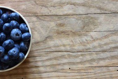 Tahta bir masada taze yaban mersinleriyle dolu bir kase, doğal ve sağlıklı bir yaşam tarzını yakalıyor. Yemek, organik ve mevsimlik temalar için ideal. Üst görünüm, yüksek çözünürlüklü resim.