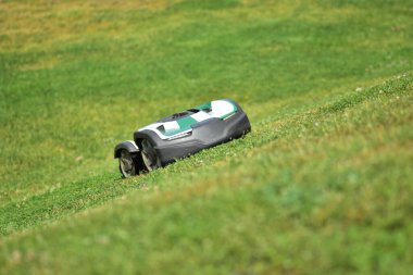 Çimenli bir tepede çalışan otonom bir robot çim biçme makinesi. Çimenlik bakımı için akıllı bahçe teknolojisi. Modern peyzaj ve açık hava bakımı için çevre dostu, zaman tasarrufu çözümü.