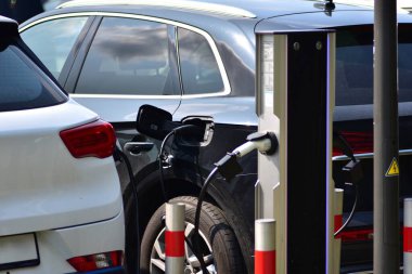 Otoparktaki şarj istasyonuna takılmış iki elektrikli araç. Temiz enerji ve çevre dostu ulaşım kavramı modern EV altyapısı ve kentsel alanlarda sürdürülebilirliği sergiliyor.