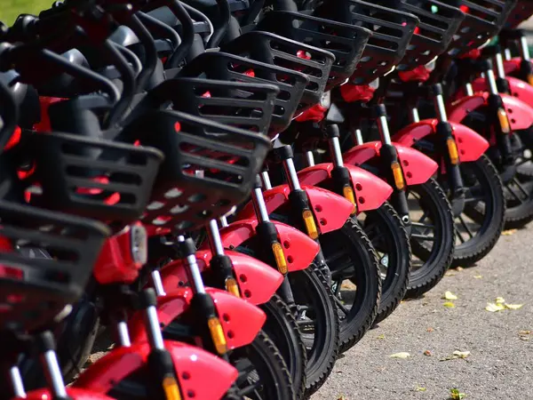 Yol kenarına düzgün park edilmiş kırmızı elektrikli scooter 'lar. Sürdürülebilir şehir taşımacılığı, mikro hareketlilik ve çevre dostu kişisel taşıma araçları ile modern şehir ulaşımı.