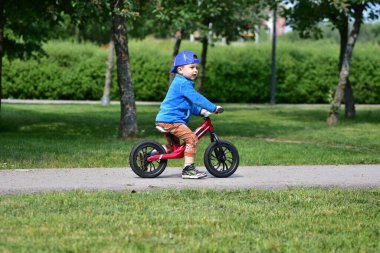 Park yolunda denge bisikleti süren küçük bir çocuk. Şapka takan ve spor kıyafetli çocuklar güneşli bir günde dışarıda eğlenmekten ve fiziksel aktivitelerden hoşlanırlar..