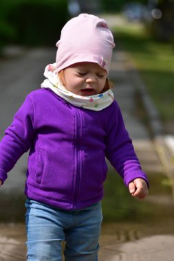 Renkli kıyafetler giymiş küçük bir kız güneşli bir günde dışarıda hapşırıyor. Çocukluğun doğal samimi anı. Sıcak hava ortamında sağlık ve mevsimsel alerji teması..