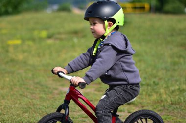 Parktaki çimlerin üzerinde bisiklete binen küçük çocuk. Kask takan ve spor kıyafetler giyen çocuk güneşli bir günde dışarıda eğlenmekten ve fiziksel aktivitelerden hoşlanır..