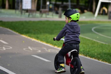 Bisiklet parkında dengeli bisiklet süren küçük bir çocuk. Kask takan ve spor kıyafetler giyen çocuk güneşli bir günde dışarıda eğlenmekten ve fiziksel aktivitelerden hoşlanır..