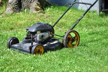 Eski benzin itme çim biçme makinesi taze kesilmiş yeşil çimlerin üzerinde duruyor. Yazın bahçe sahnesi. Vintage bahçe bakım ekipmanları. Kırsal yaşam kavramı ve elle yetiştirilen çimen bakımı.