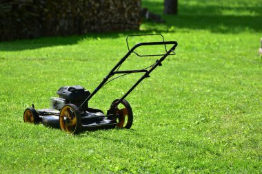 Eski benzin itme çim biçme makinesi taze kesilmiş yeşil çimlerin üzerinde duruyor. Yazın bahçe sahnesi. Vintage bahçe bakım ekipmanları. Kırsal yaşam kavramı ve elle yetiştirilen çimen bakımı.