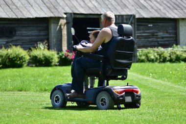 Mutlu büyükbaba, neşeli genç oğlanla birlikte elektrikli mobilete biniyor güneşli kırsal alanda kucağında, bağ kurmayı, çoklu-kuşak aşkı ve açık havada aktif yaşam tarzını gösteriyor..