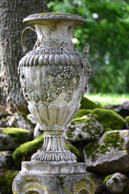 Yosun bahçesinde duran süslü, kaliteli, çiçekli bir vazo. Klasik dekoratif unsur zarafet, tarih ve romantik bahçe taşır.