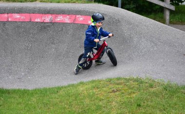 Mavi ceketli ve kasklı aktif bir genç açık hava pompa pistinde kırmızı denge bisikletine biniyor. Yeşil Park 'ta yaz günü bisiklet eğitimi alan bir çocuk. Aktif çocukluk ve spor kavramı.